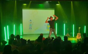 Rémi comptines les bras levés devant un grand tableau d'école