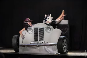 un couple dans une deux chevaux décapottée elles sont mélangés, elle porte un masque de tête de vache