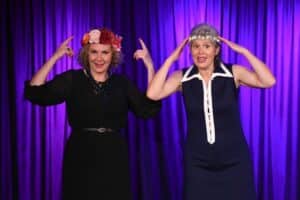 Portrait de KArine et Corinne dans le spectacle coméique "Entrez dans la transe", elles sont debut les mains dirigées vers leur tête, l'air amusé