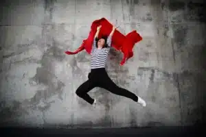 portrait d'Olivia Moore saute en l'air avec un foulard rouge dans les mains devant un mur bétonné