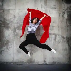 portrait d'Olivia Moore saute en l'air avec un foulard rouge dans les mains devant un mur bétonné