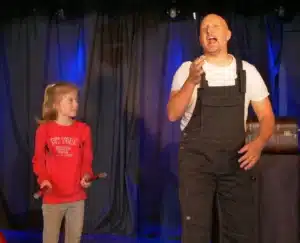 Philibert le magicien parle au public avec une petite fille près de lui