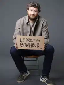 Olivier de Benoist, assis avec un carton où est écrit "Le droit au bonheur" entre les mains