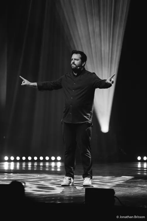 Photo de Kostia ennoir et blanc. Debout sur scène, bras écartés