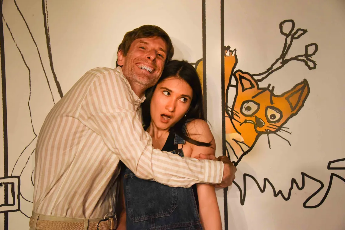 Photo de scène "Ado un jour, à dos toujours" : un homme en pull enlace en souriant une jeune femme qui cherche à s'enfuir