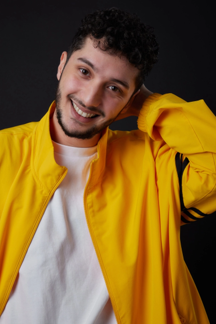 Portrait d'Elies Zoghlami souriant, chemise blanche blazer jaune, main derrière la tête