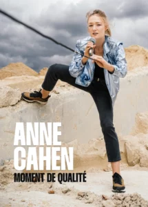 Affiche de Anne Cahen dans Moment de Qualité. Un micro à la main debout sur des pierres, elle tire sur le fil du micro.