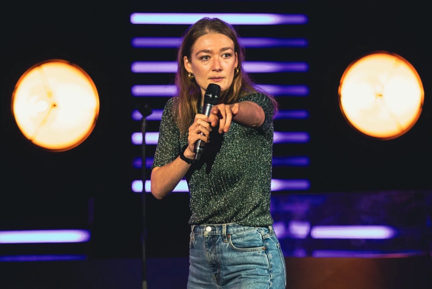 Anne Cahen en spectacle; de face, un micro à la main, elle pointe le doigt en avaznt
