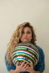 Camille Tissot boudeuse, en photo, une boule à facettes multicolores dans les bras