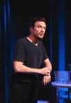 Photo de Guillaume Guisset dans son seul en scène, l'air inquiet, debout, tee-shirt noir