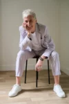Photo portrait de Marie Bô, assise sur un tabouret, souriante, en costume perle