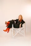 Photo d'Olympe assise en travezrs sur un fauteuil de réalisateur, habillée de noir, bottines rouges